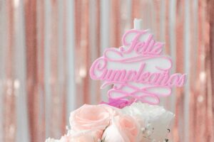 Close-up of a birthday cake with pink roses and a festive 'Feliz Cumpleaños' topper.